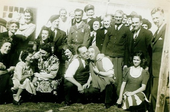 Odella (far left, in front of baby), Eglantine (kneeling below Odella, wearing light print dress), Mamie (top middle, wearing military hat), Henry (wearing sweater with tie), Frank (to Henry's left). Photo taken in 1944, in front of Henry's house at 4 Mill Circle.